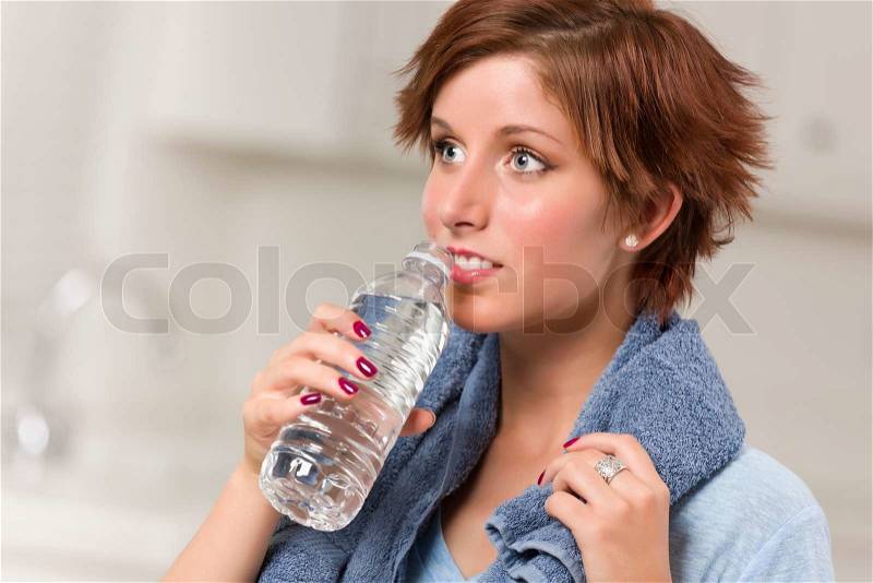 Pretty Red Haired Woman with Towel Drinking From Water Bottle in Her Kitchen, stock photo