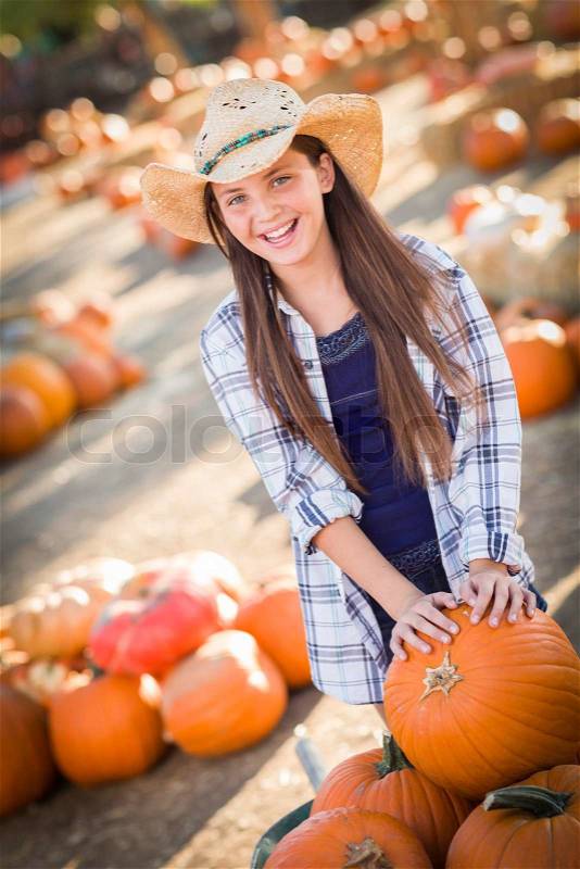 Preteen Girl Wearing Cowboy Hat Playing with a Wheelbarrow at the Pumpkin Patch in a Rustic Country Setting. , stock photo