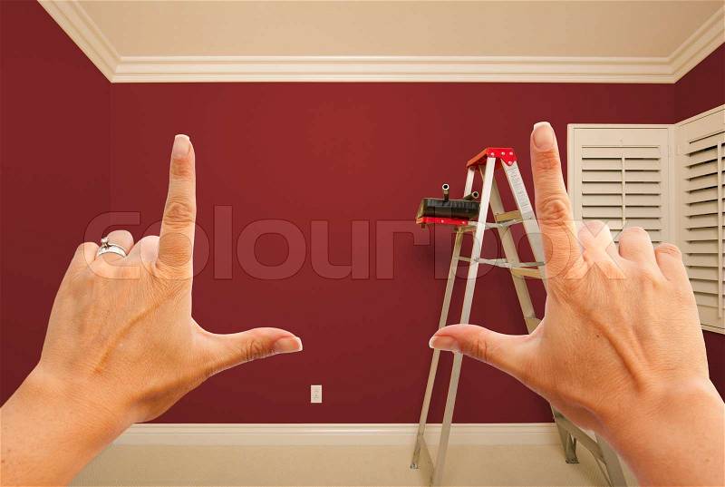 Hands Framing Deep Red Painted Room Wall Interior with Ladder, Paint Bucket and Rollers, stock photo