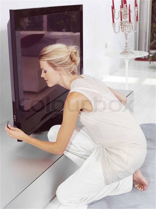 Beautiful blond woman sitting near tv and tries to connect compact chip, stock photo