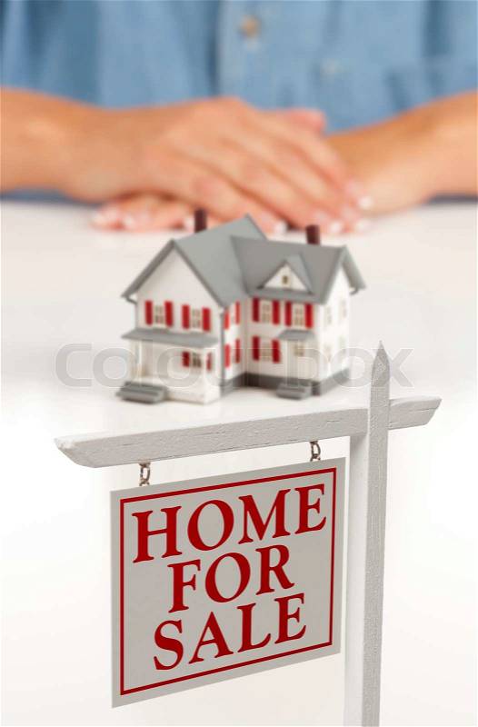 Womans Folded Hands Behind Model House and Home For Sale Real Estate Sign In Front on White Surface, stock photo