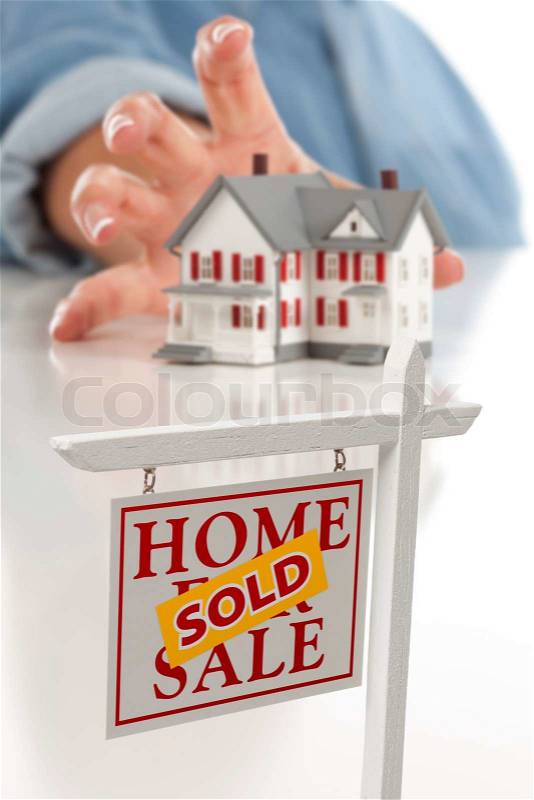 Sold Real Estate Sign in Front of Womans Hand Reaching for Model House on a White Surface, stock photo