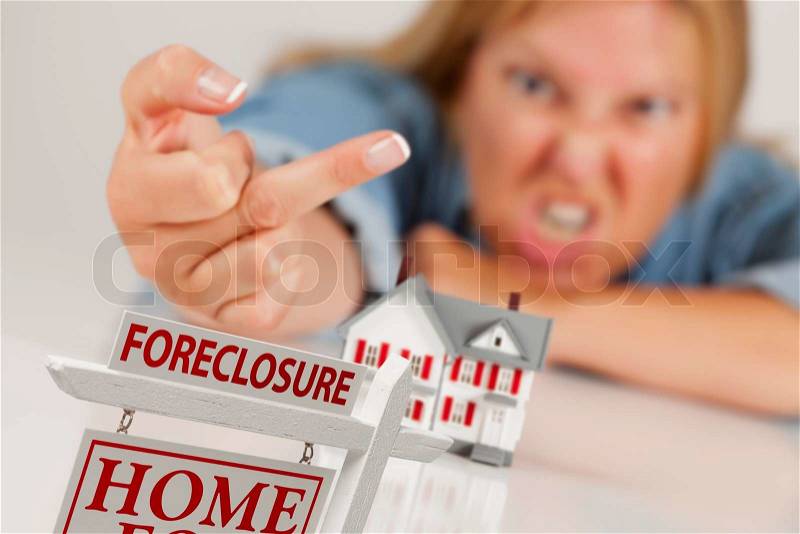 Angry Woman Flipping The Bird Behind Model Home and Foreclosure Real Estate Sign in Front, stock photo