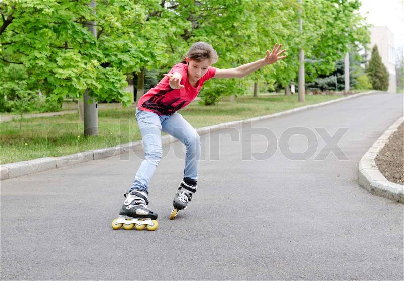 Attractive teenage girl roller skating on roller blades on a tarred rural road rounding a bend at speed with her arms flying, stock photo