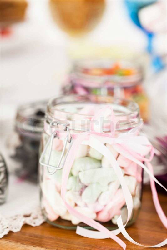 Closeup of pastel colored marshmallows in glass jar with decorative ribbon tied in bow, stock photo