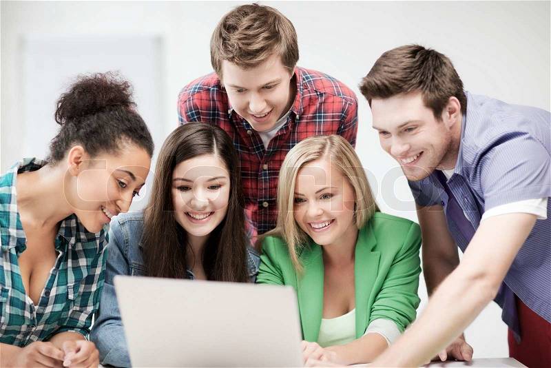 Education and internet concept - group of international students looking at laptop at school, stock photo