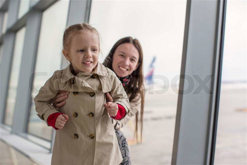 Mother and little daughter looking out the window at the airport terminal, stock photo