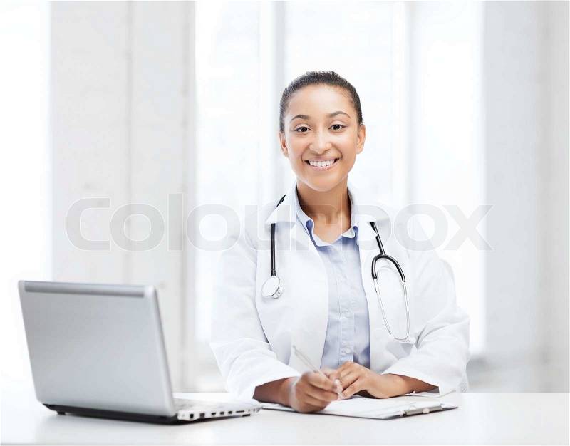 Healthcare, medical and technology concept - african female doctor with laptop pc writing prescription, stock photo