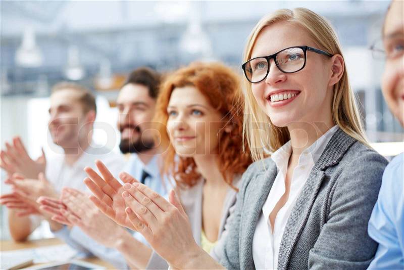 Group of happy business people applauding at conference with smiling blonde in front, stock photo