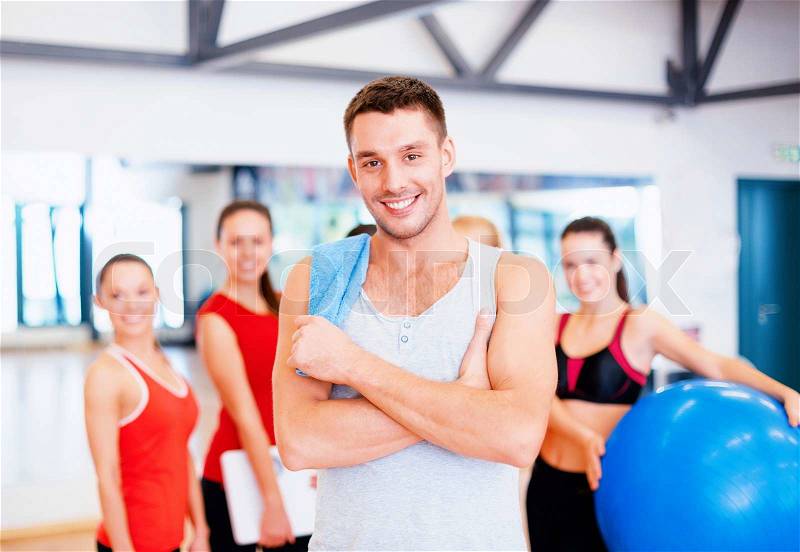 Fitness, sport, training, gym and lifestyle concept - smiling man standing in front of the group of people in gym, stock photo