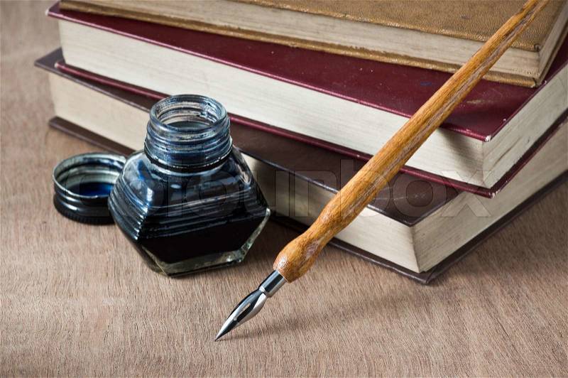 Still life photography, vintage books are stacked on wooden table with dip pen and inkwell, stock photo