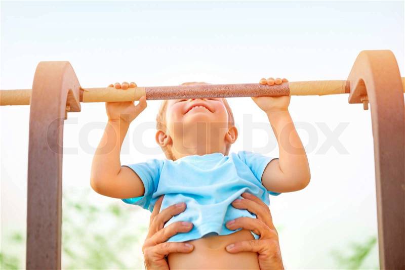 Little boy with fathers help catch up on the horizontal bar, active childhood, cute small acrobat, workout on backyard, summer camp concept, stock photo