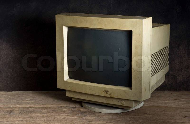 Old computer monitor on old wood table on dark background, stock photo