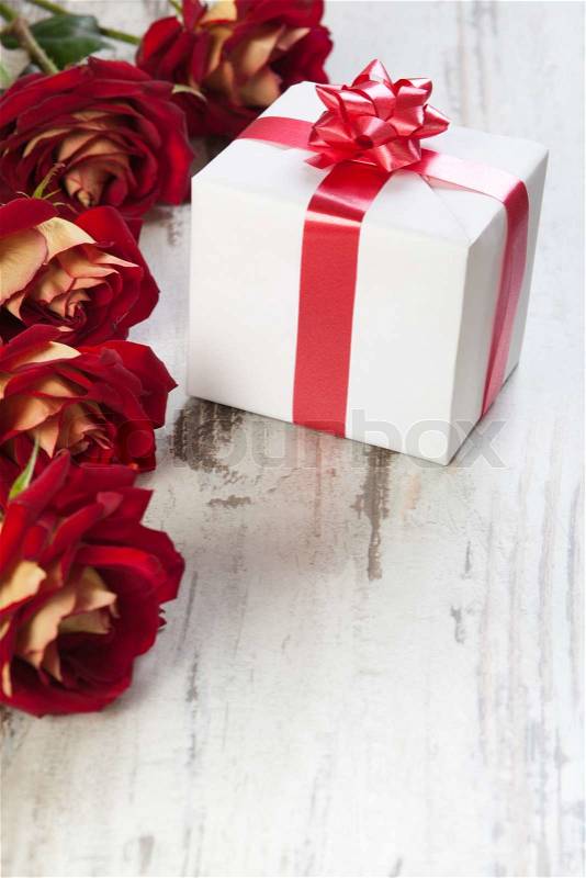 Gift box with red ribbon on a white board with roses, stock photo