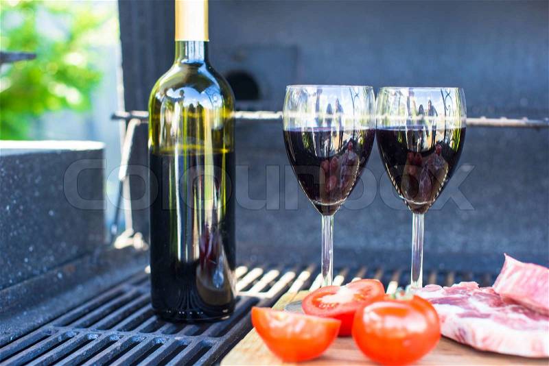 Two glass of red wine, steak and tomatoes on barbecue outdoors, stock photo