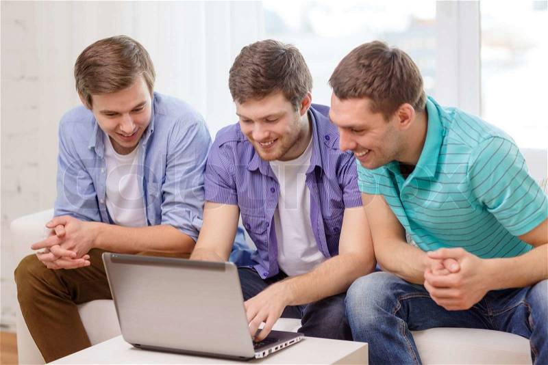 Friendship, technology and home concept - smiling male friends with laptop computer at home, stock photo