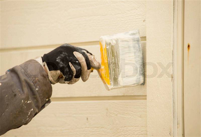 An arm holding a brush and painting an exterior wall, stock photo